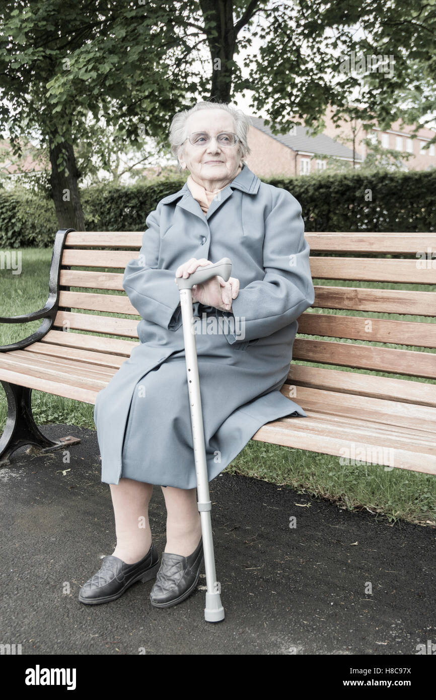 89 ans femme assis sur un banc dans un parc public. UK Banque D'Images