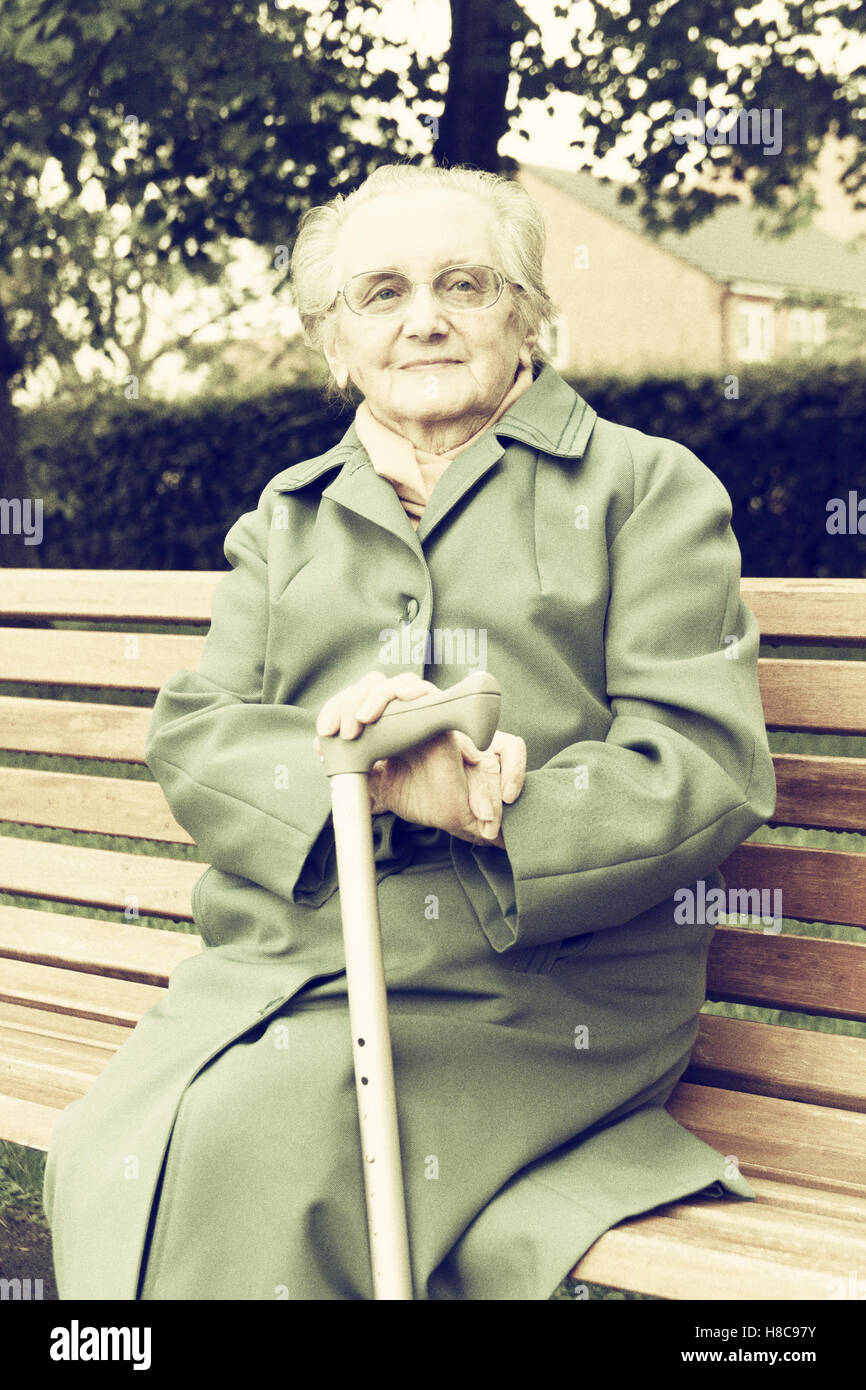 89 ans femme assis sur un banc dans un parc public. UK Banque D'Images