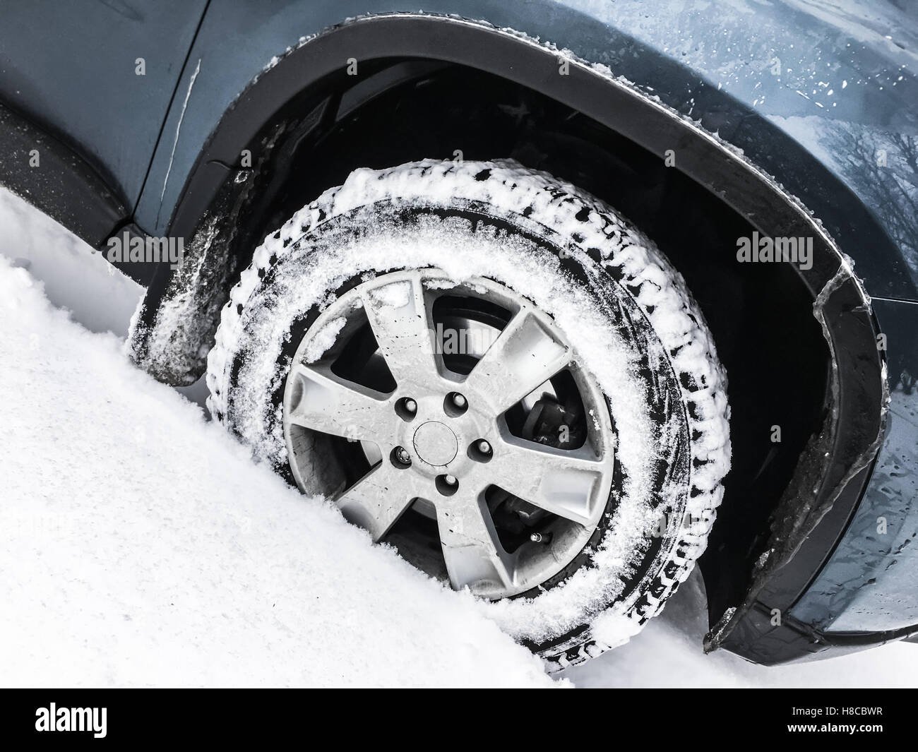 Voiture bleue moderne fragment, roue à pneu clouté debout sur la route d'hiver avec de la neige profonde Banque D'Images