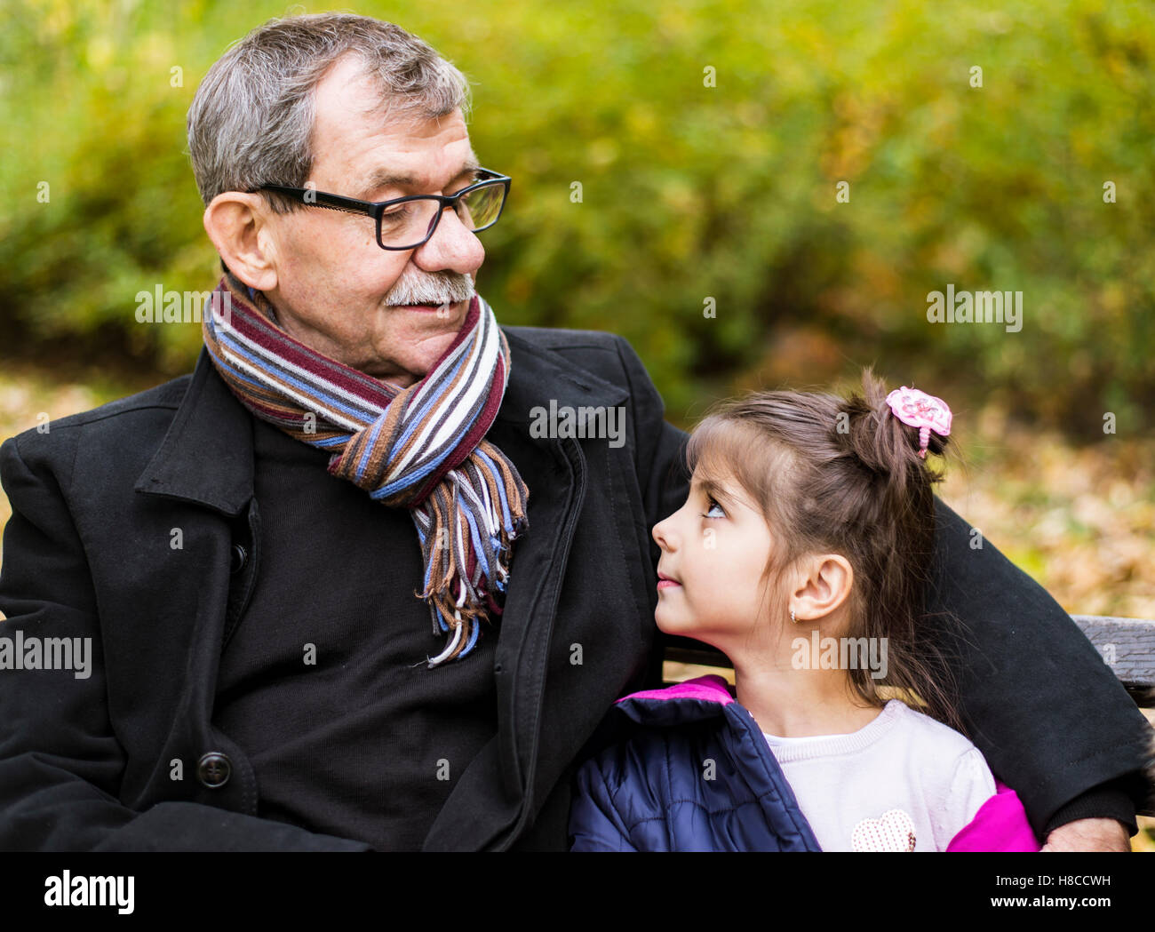 Petite fille et son grand-père assis sur un banc dans le parc en automne Banque D'Images