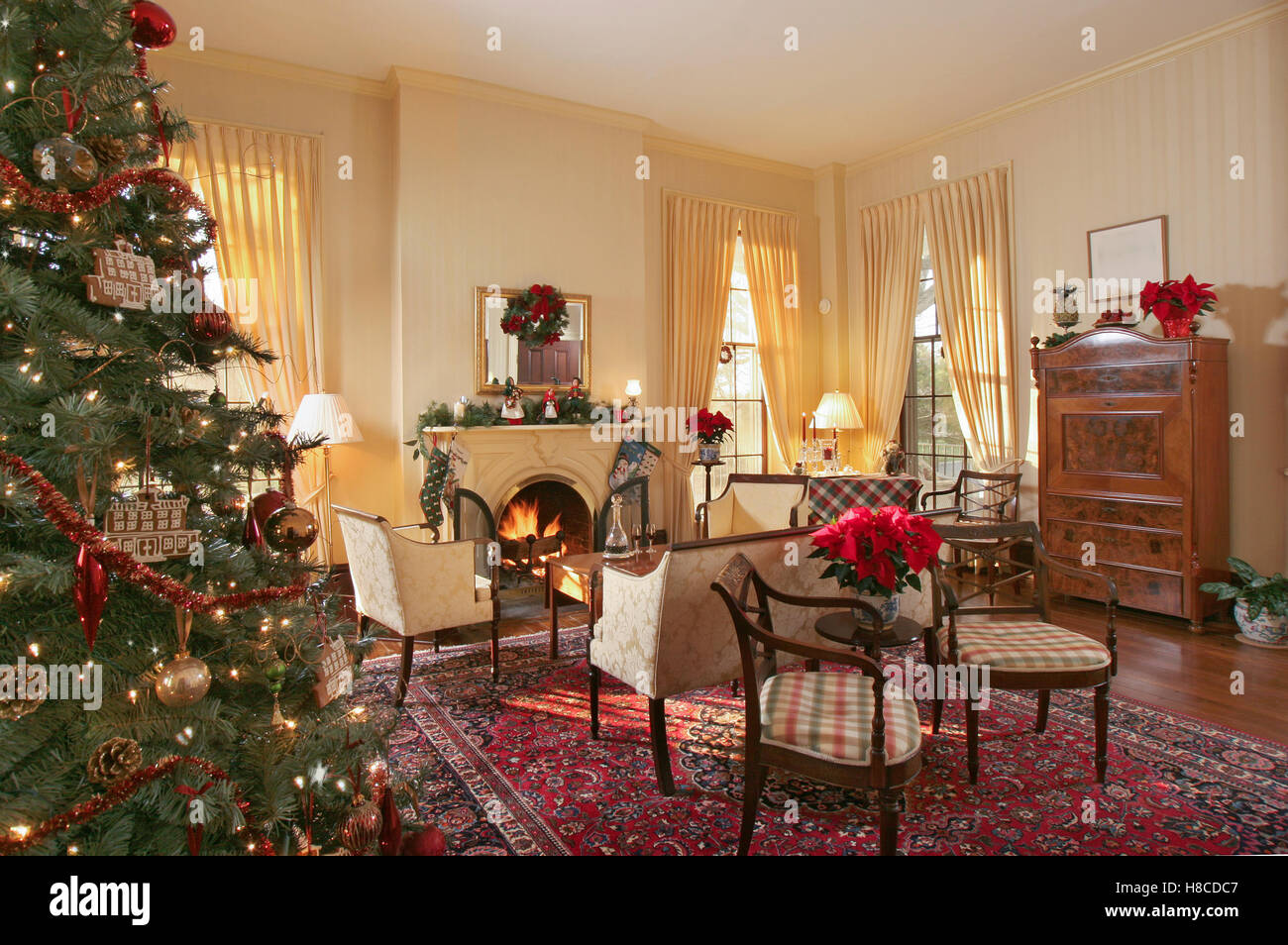 Chaises rembourrées devant le foyer avec le feu allumé dans la salle de séjour décorée pour Noël. Banque D'Images
