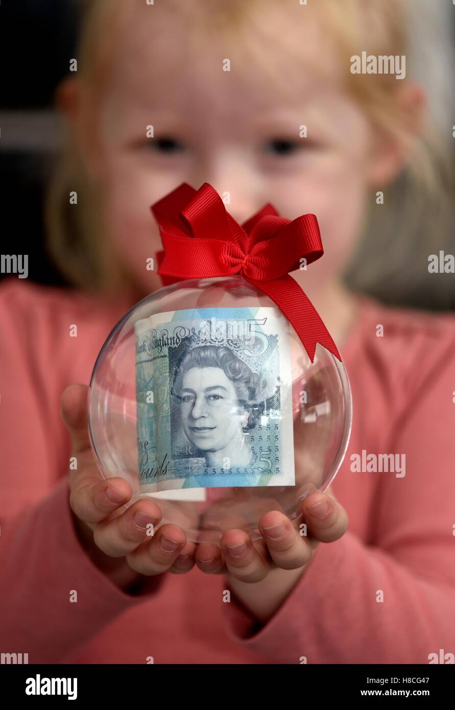 Un bébé fille tenant une boule de Noël avec une note de cinq livres à l'intérieur. Banque D'Images