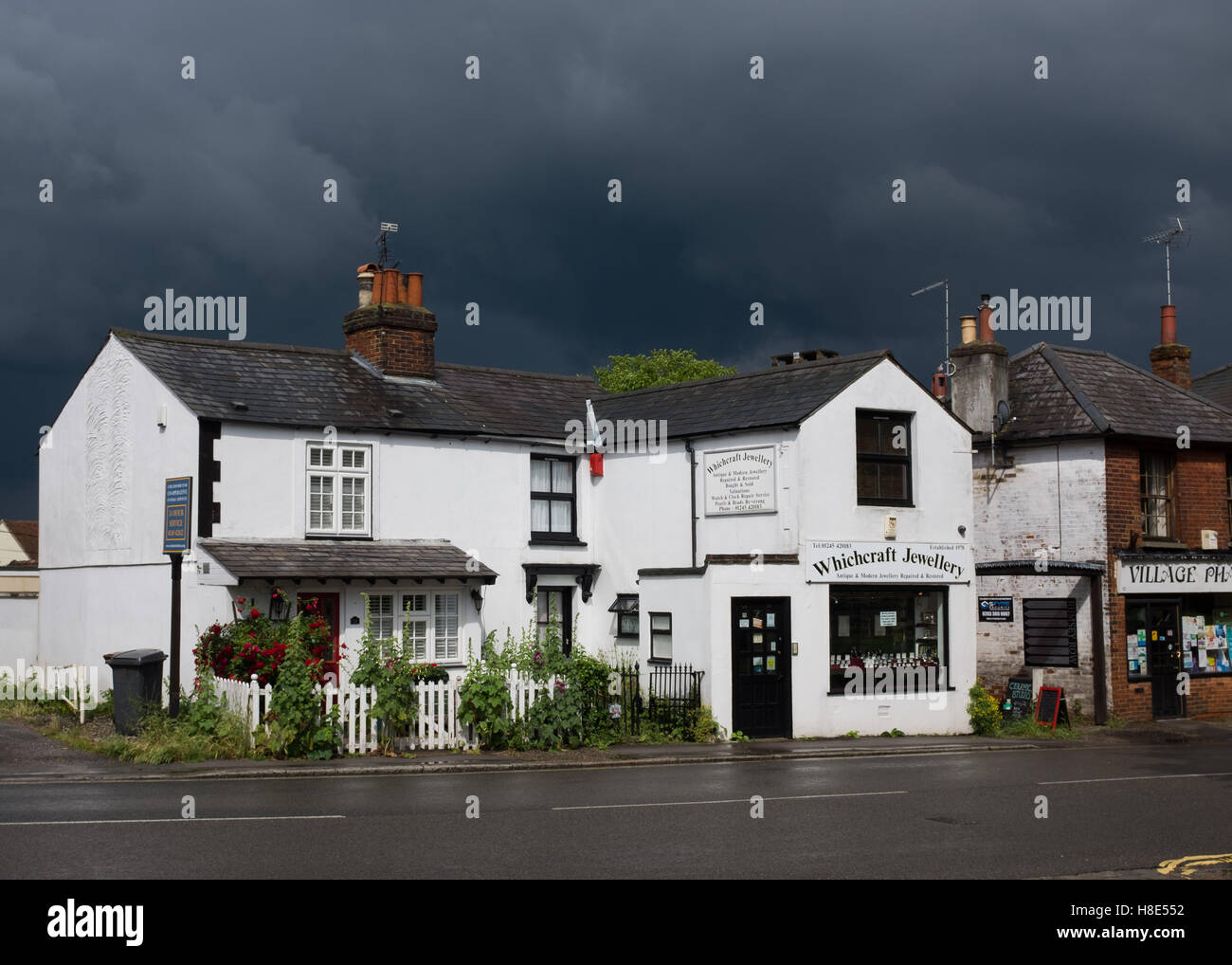 Les nuages de tempête sombre dans le ciel au-dessus de white cottages en Essex, Angleterre. Banque D'Images