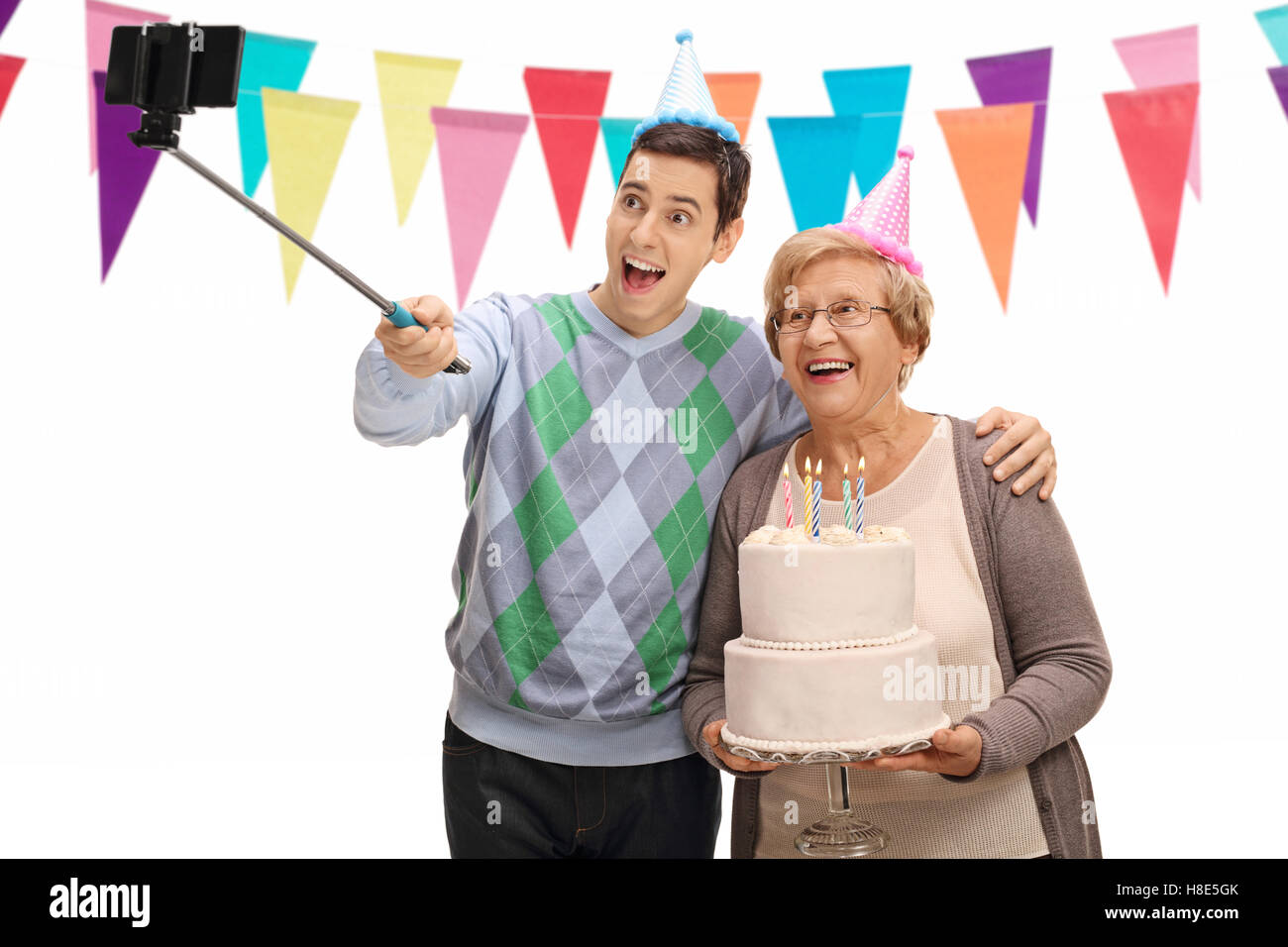 Jeune homme et une femme mature avec des chapeaux de fête et un gâteau d'anniversaire en tenant un bâton avec un selfies isolé sur fond blanc Banque D'Images