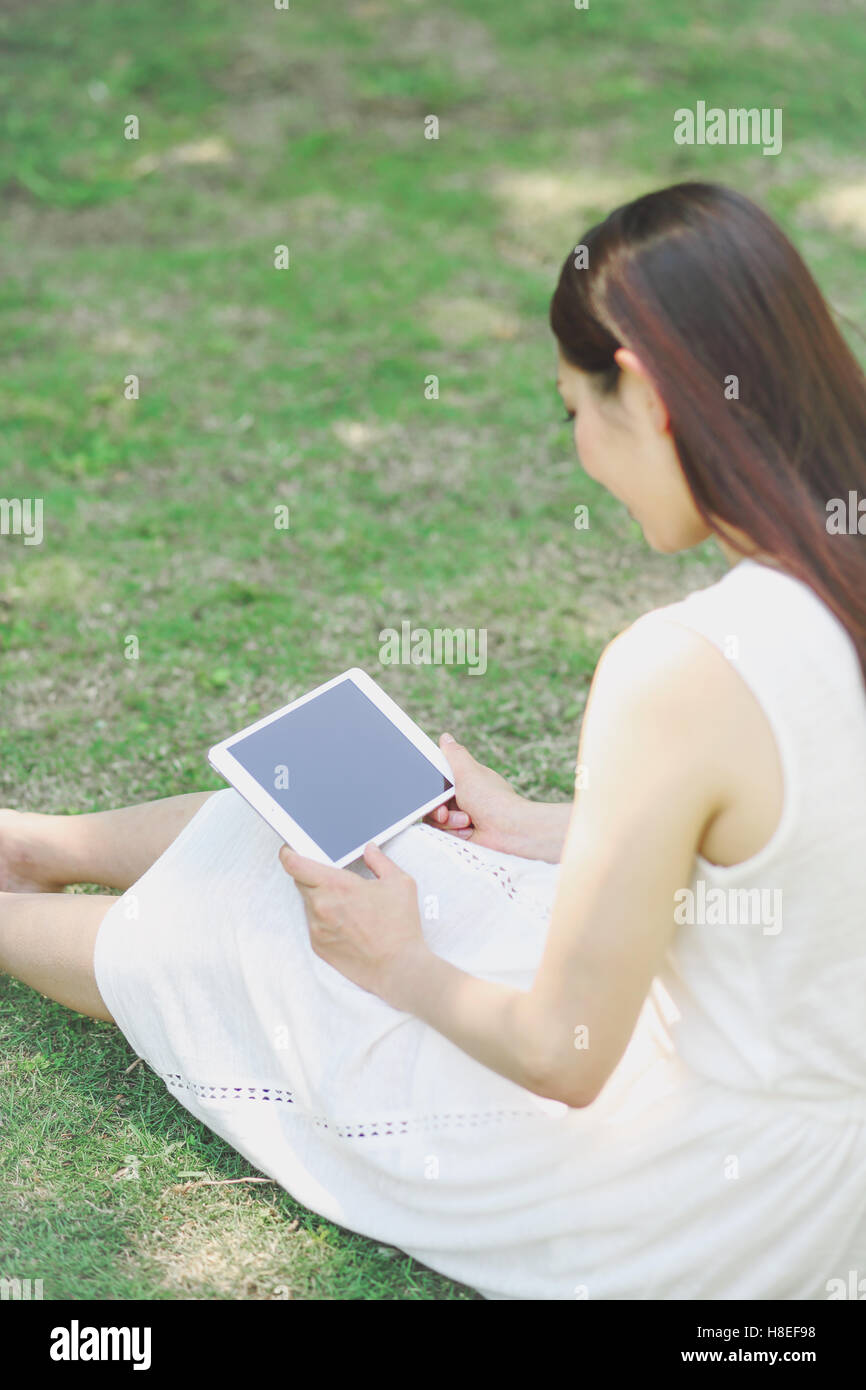 Portrait de jeune japonaise portant sur l'herbe avec tablet Banque D'Images