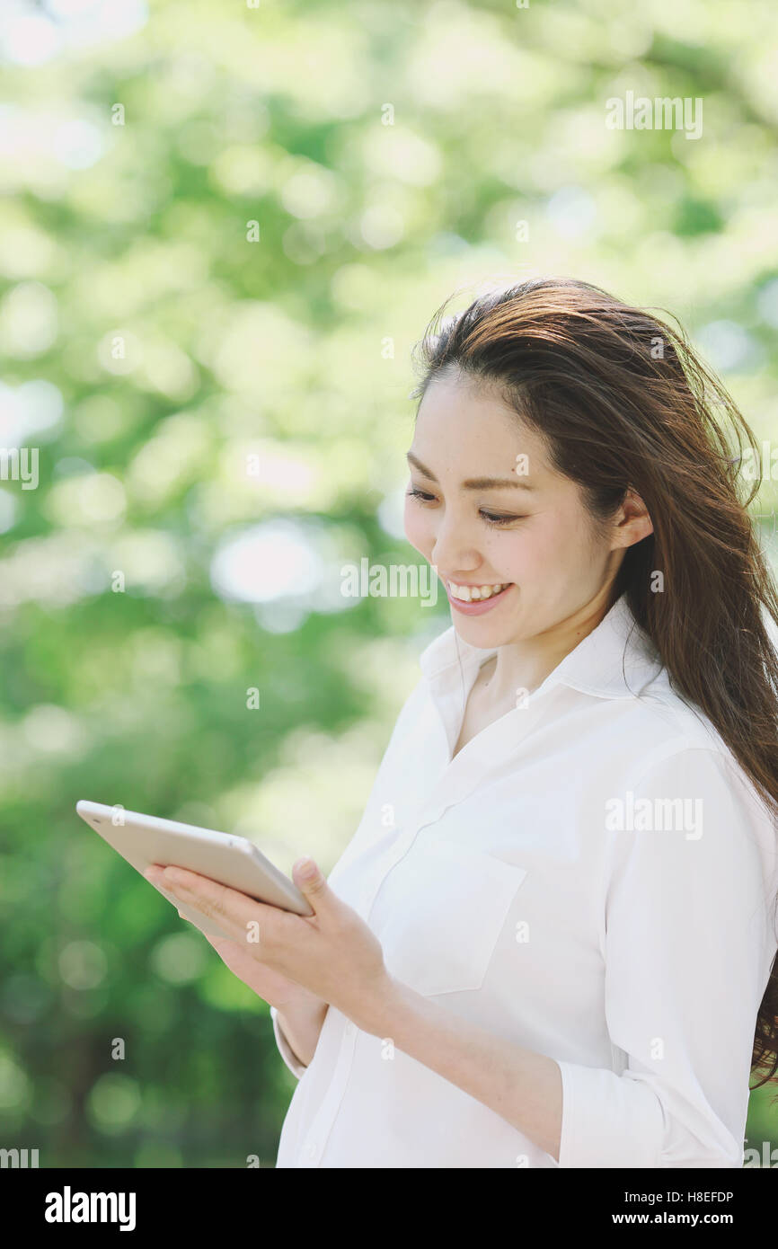 Jeune japonaise avec tablet entouré de verdure dans un parc de la ville Banque D'Images