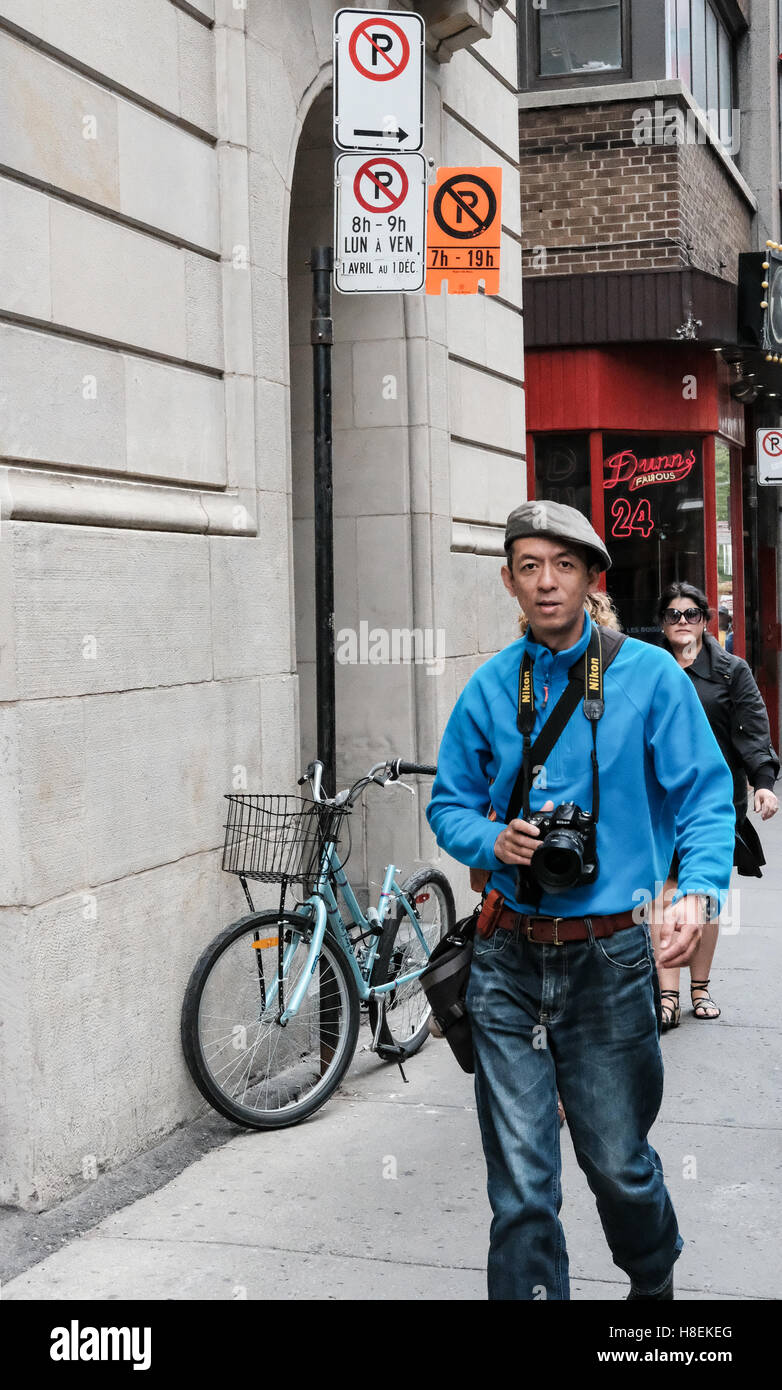 Photographe vu de ses vêtements et accessoires appareil photo reflex en descendant un trottoir dans un centre-ville. Banque D'Images