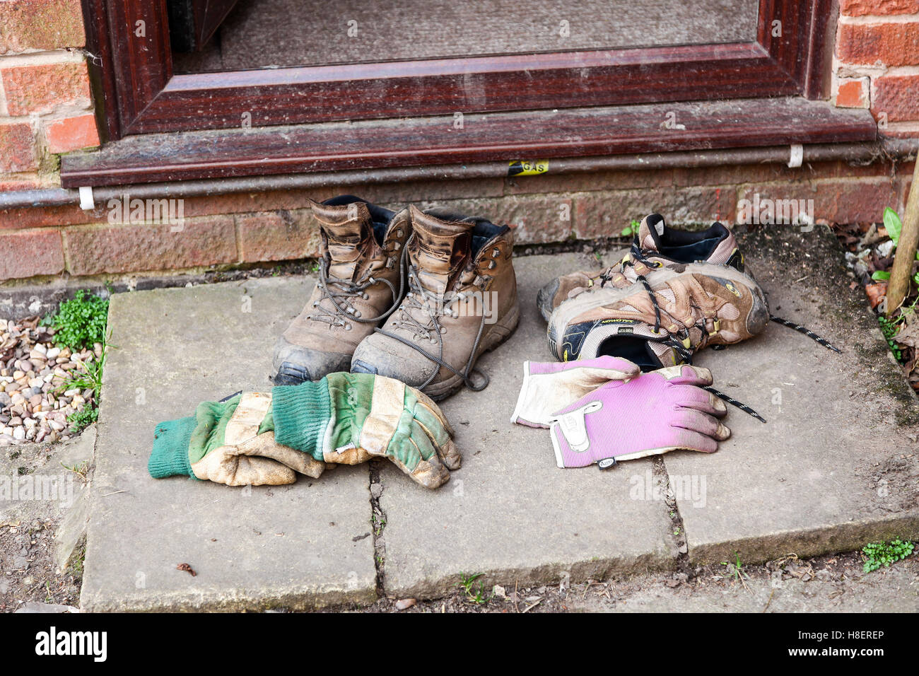 Une paire de vieux mens bottes et des gants de jardinage et d'une paire de gants de jardinage et de formateurs de womans sur la porte arrière de l'étape Banque D'Images