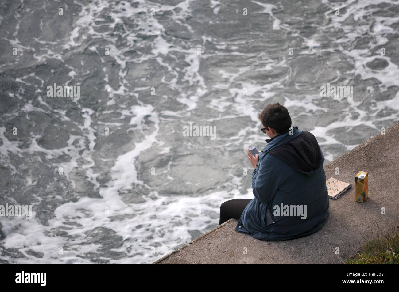 Un étudiant assis sur la digue à Falmouth, Cornwall. Banque D'Images