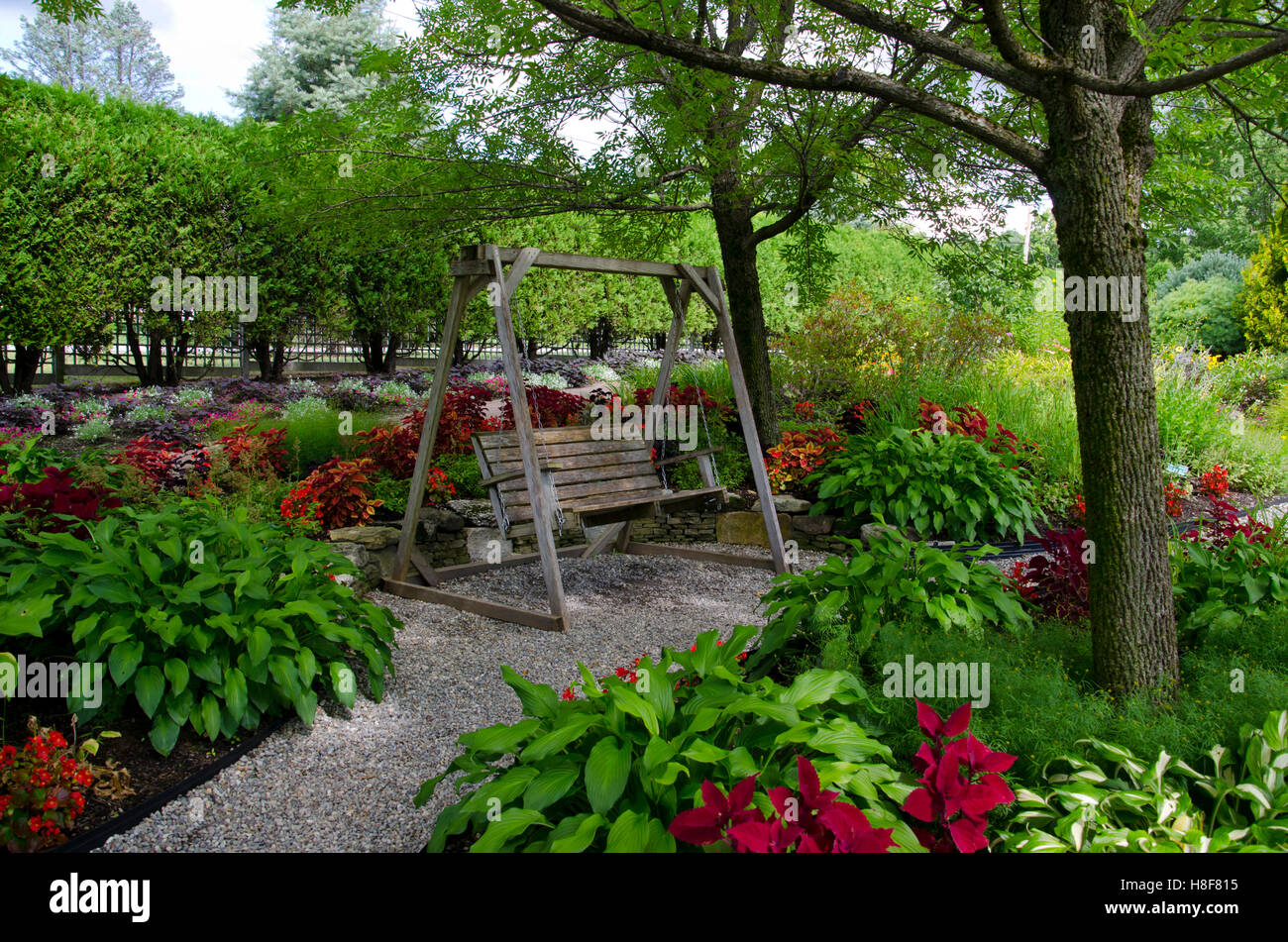 Balançoire en bois siège à Pineland jardin avec des hostas et coléus dans l'ombre le long chemin de gravier, nouveau Gloucester, Maine, USA Banque D'Images