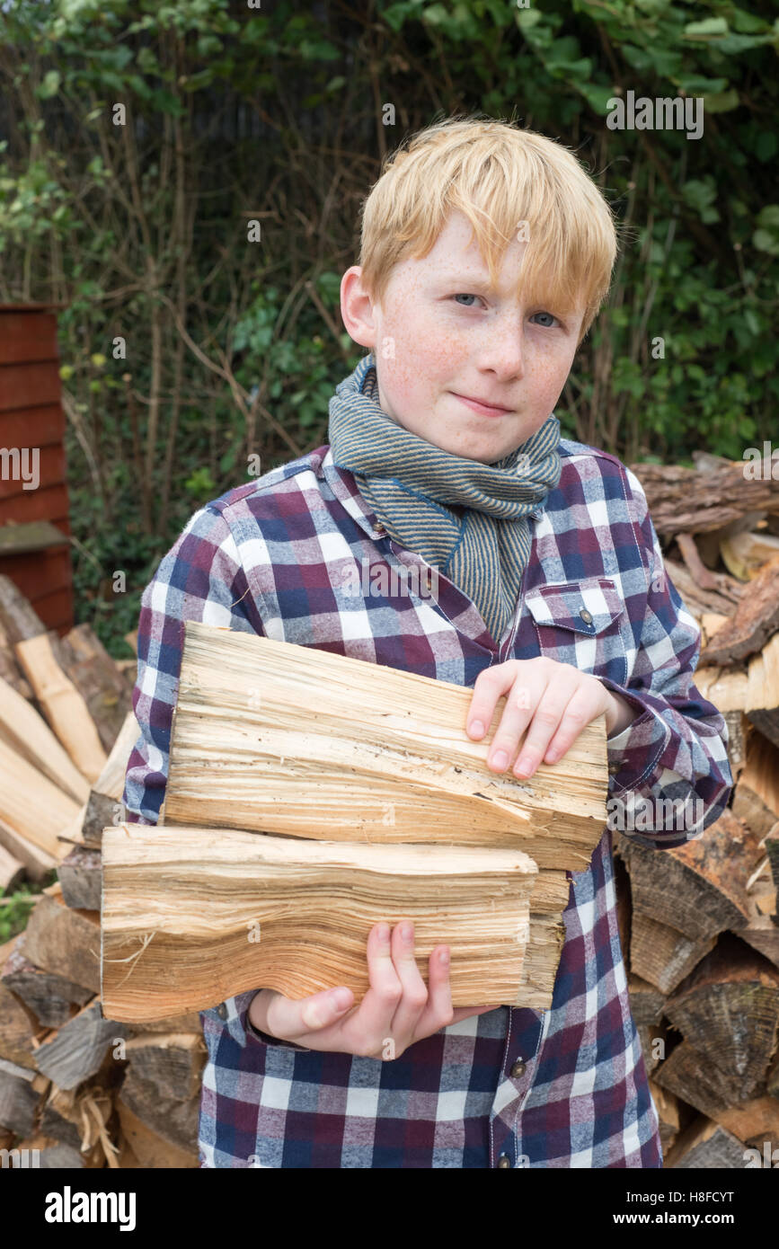Garçon en chemise à carreaux, un foulard, et hat holding une hache en face d'un tas de bois de chauffage dans une ferme Banque D'Images