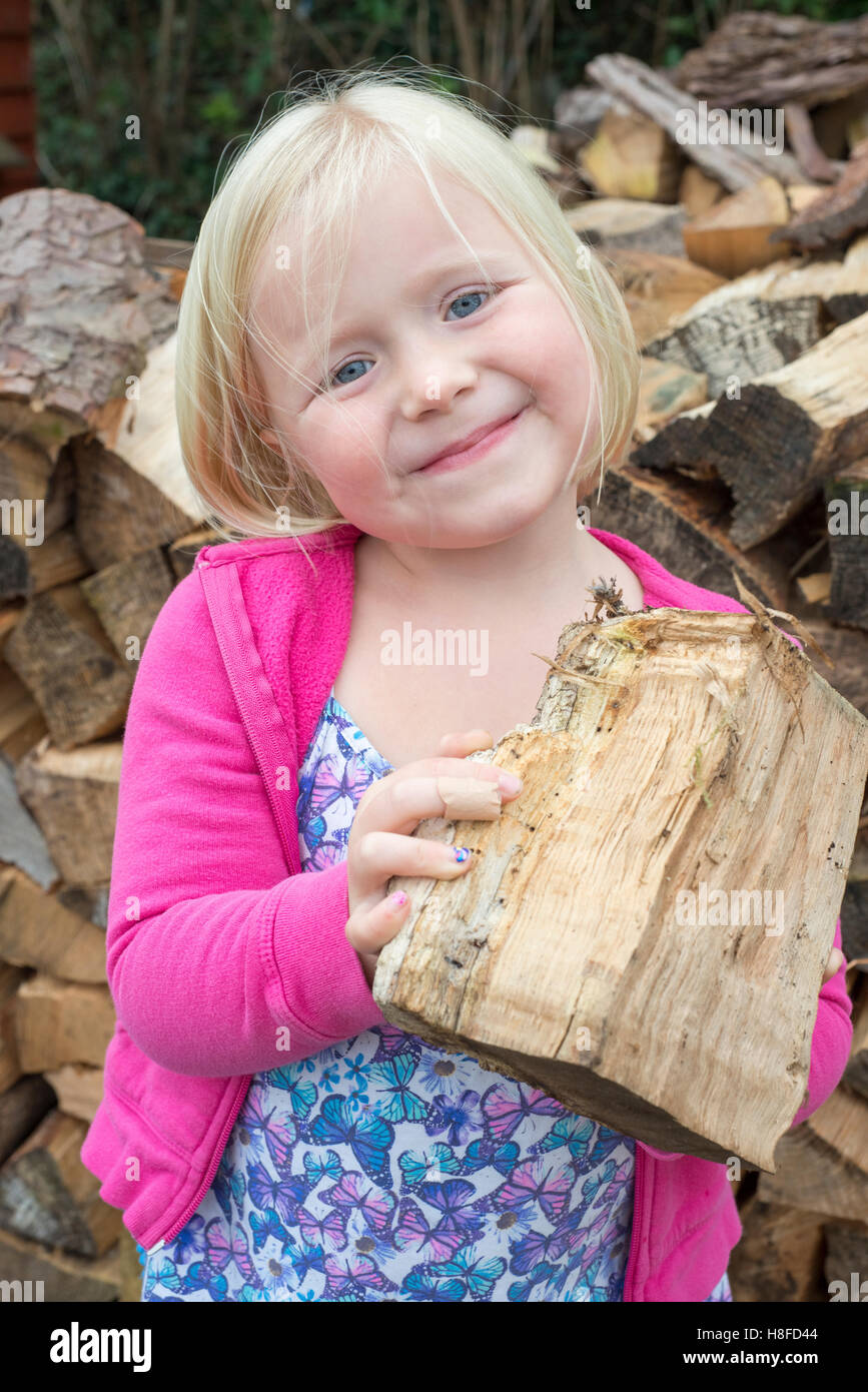 Little girl smiling, un morceau de bois de chauffage Banque D'Images