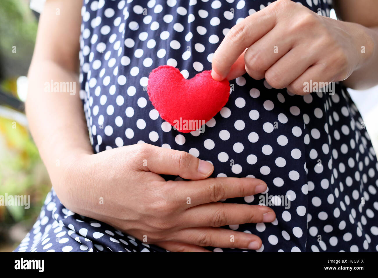 Les femmes enceintes porter des vêtements de maternité bleu marine et un cœur rouge signes figurant sur le ventre. Banque D'Images