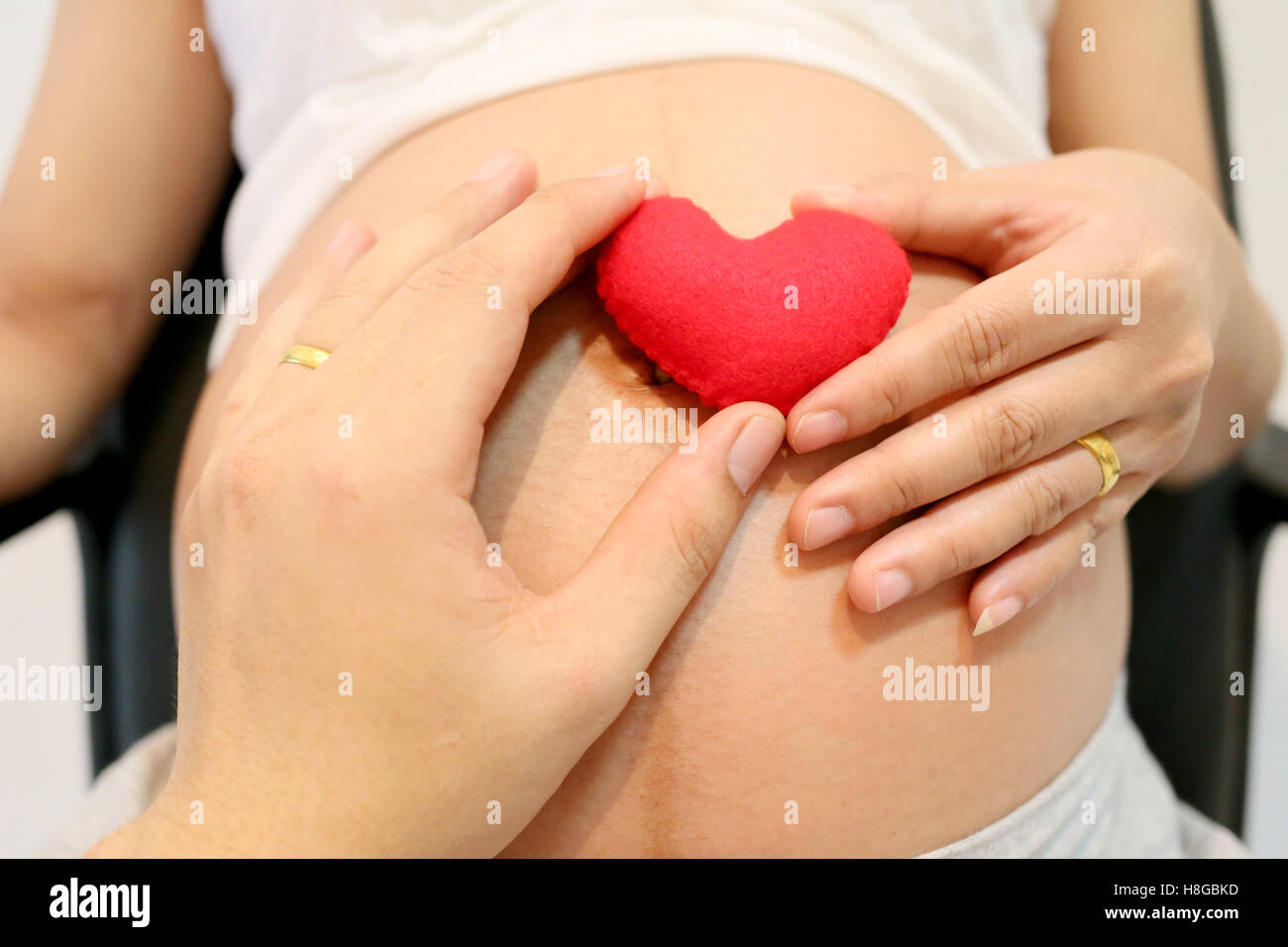Les femmes enceintes la main et mari part garder un cœur rouge signes figurant sur ventre concept d'amour pour le bébé. Banque D'Images