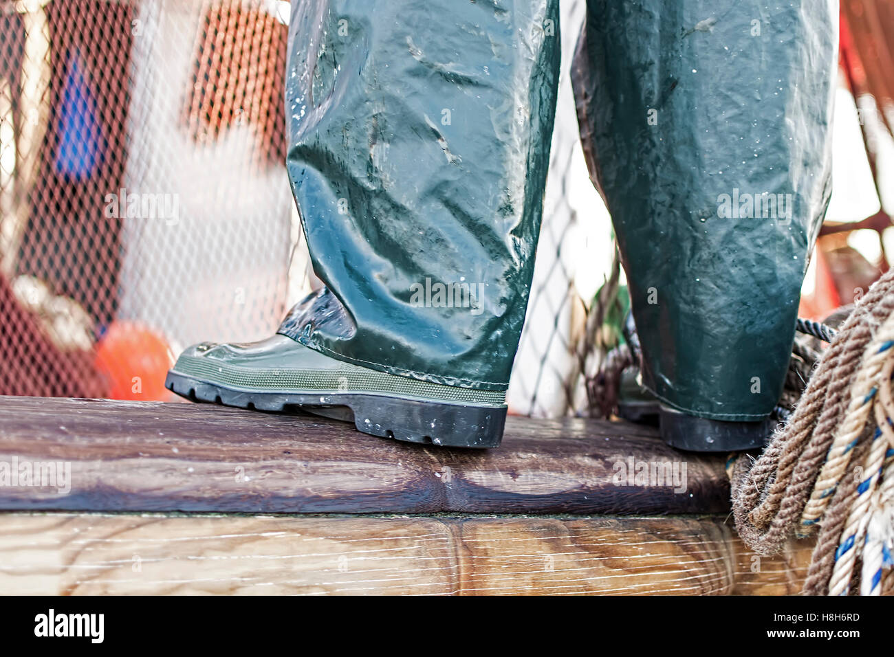 Pêcheur debout sur le bord de la bateau en bois. Bottes de pêcheurs de vert avec des filets et des cordes à l'arrière-plan. Banque D'Images