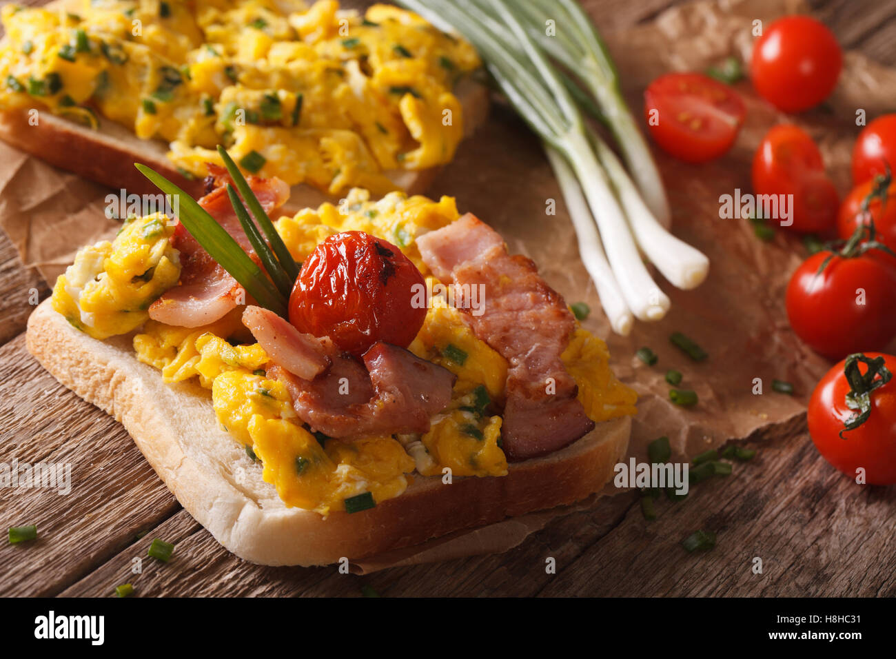 Sandwich fait maison avec des œufs brouillés, bacon et les tomates sur la table horizontale. Banque D'Images