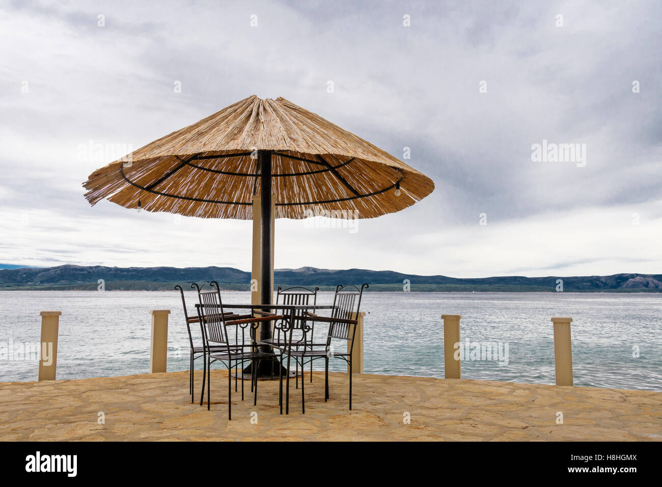 Terrasse au bord de la mer avec des chaises, table et parasol de paille, de  la mer et une île dans l'arrière-plan Photo Stock - Alamy