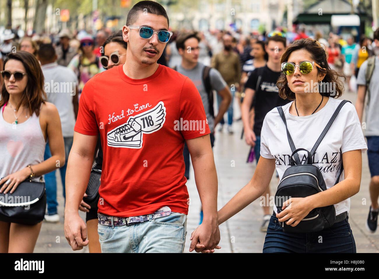 Deux touristes, un homme et une femme, portant des lunettes de soleil, à pied avec la foule de gens le long de la Rambla de walking street. Banque D'Images
