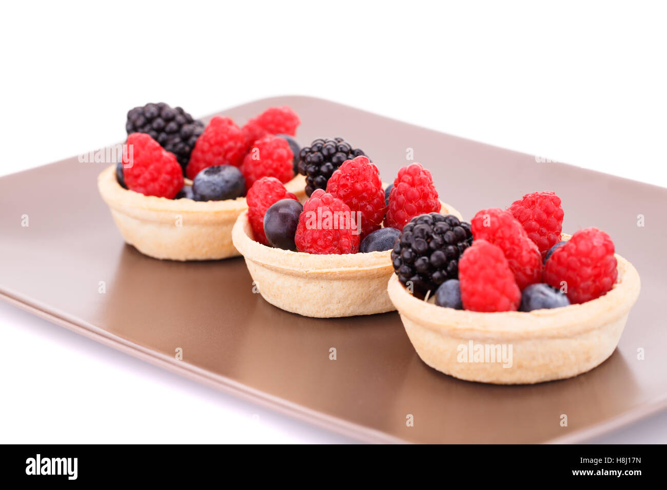 Tartelettes aux fruits frais mûrs dans sur la plaque brune. Banque D'Images