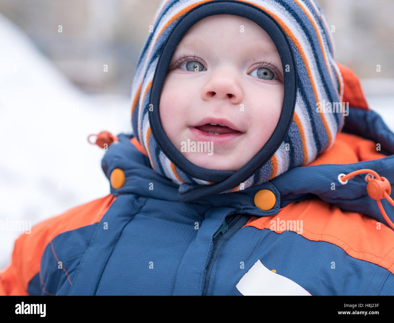Joli Bébé Garçon jouant avec la première neige. Il sourit et regarde  bonhomme de neige. Bleu épais-combinaison orange à rayures lumineuses hat  sur un ans Photo Stock - Alamy