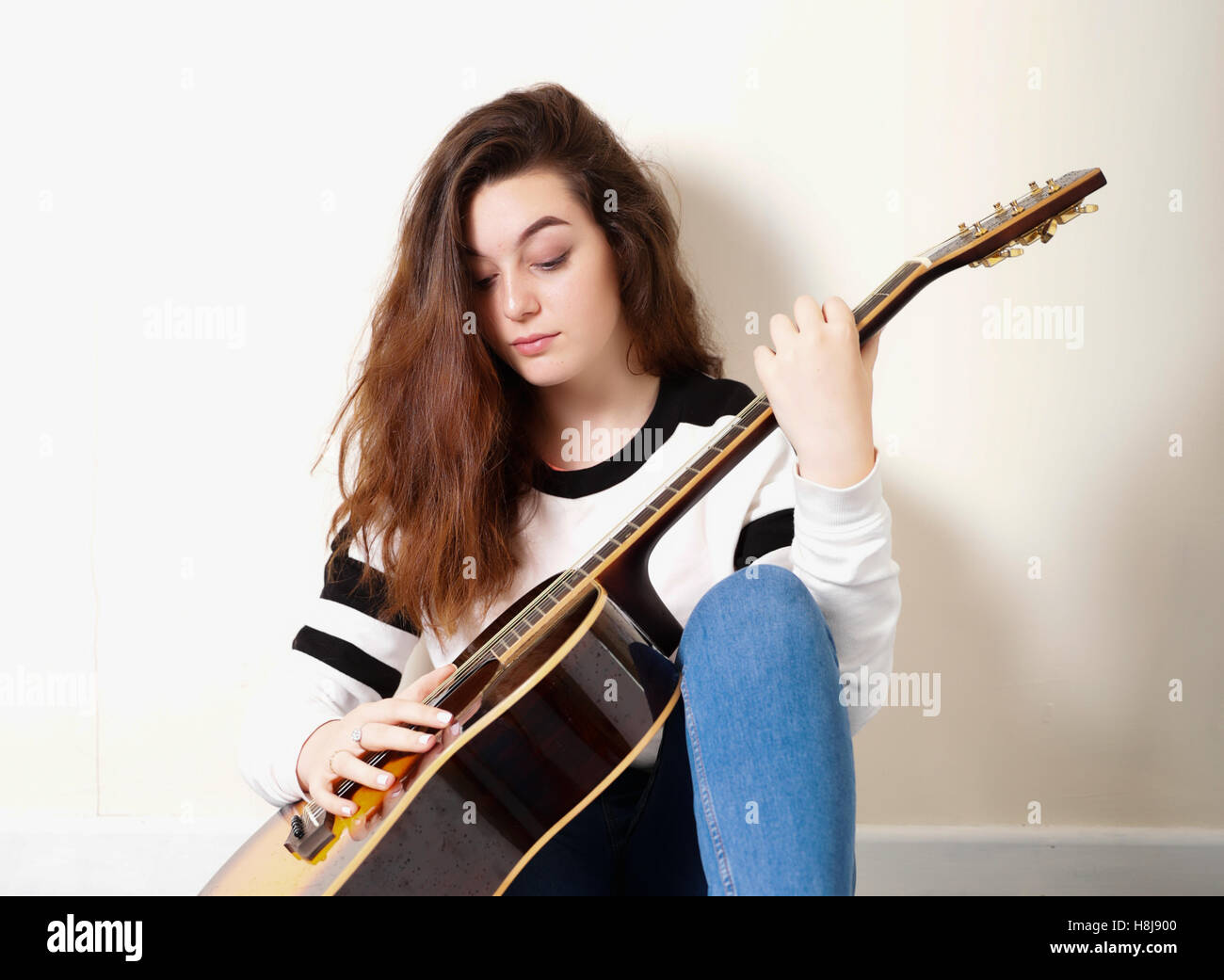Adolescente avec une guitare acoustique appuyé contre un mur à l'intérieur Banque D'Images