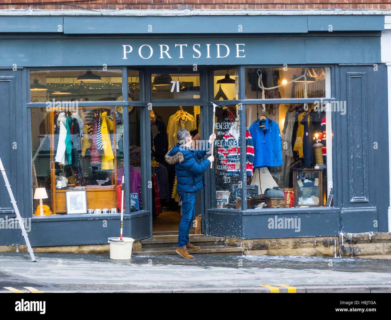 Avec l'homme et de l'eau savonneuse mops windows nettoyage et peinture sur l'avant de 'Port' d'un magasin de vêtements à Whitby Noeth Yorkshir Banque D'Images