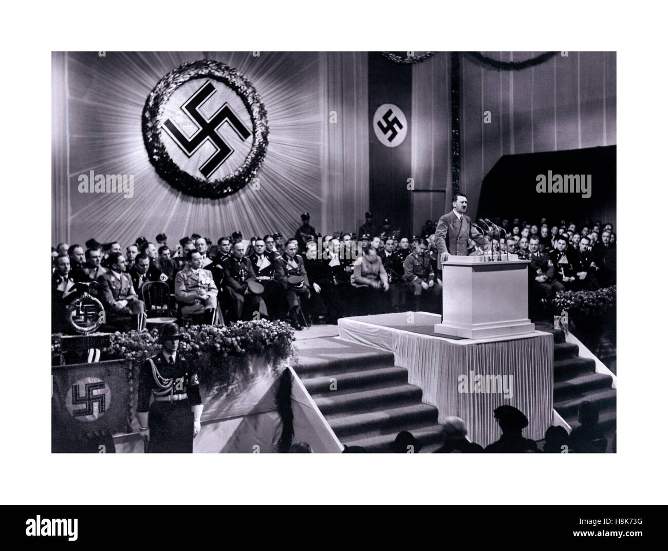 Adolf Hitler Discours, 1939 s'exprimant sous un grand emblème de la croix gammée lors d'un discours sur le podium avec d'autres partisans du parti nazi 1939 Berlin Allemagne Banque D'Images