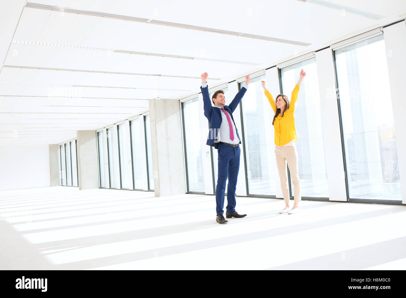 Toute la longueur d'affaires accompli et businesswoman with hands raised in empty office Banque D'Images