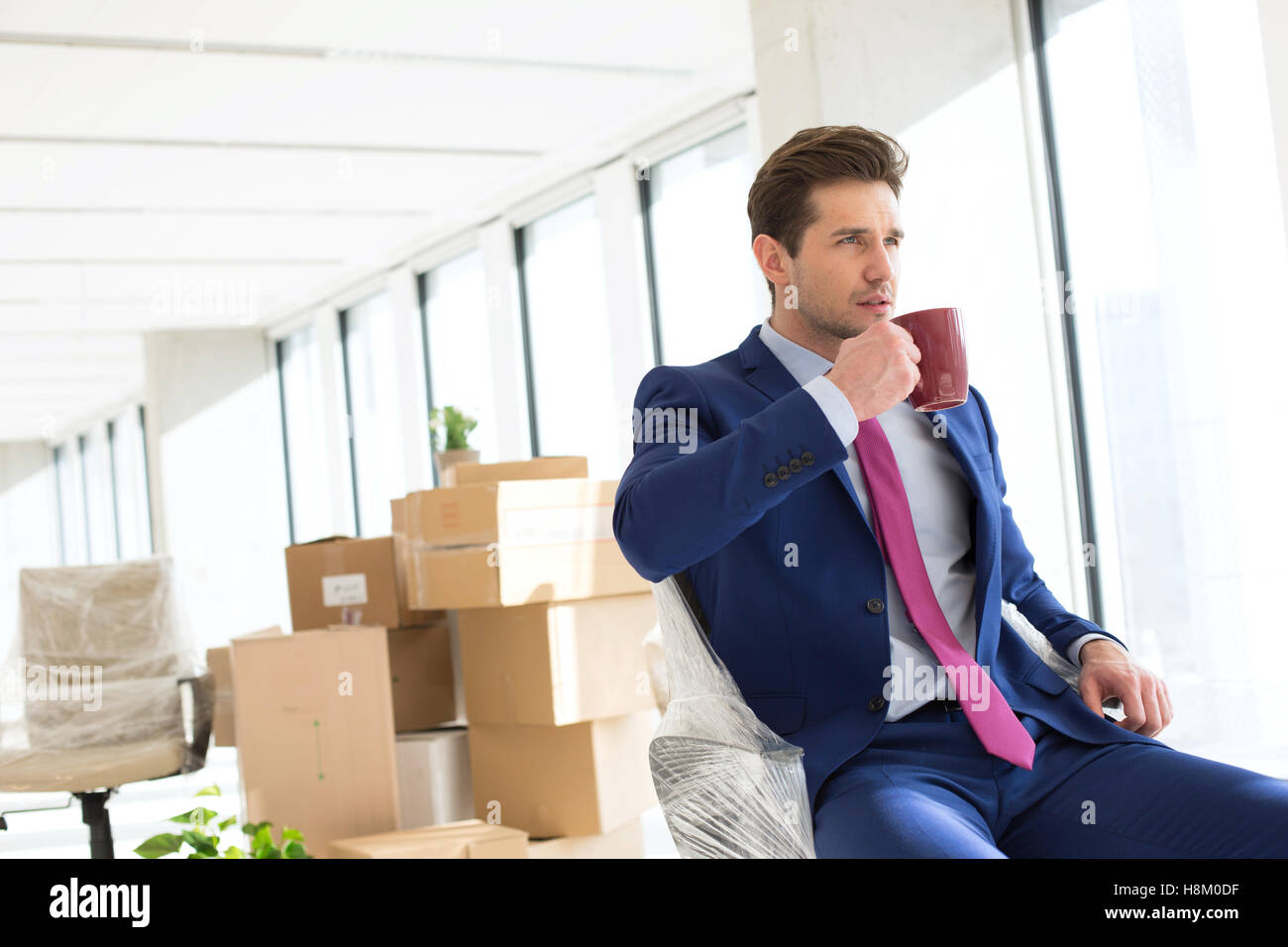 Portrait of young woman drinking coffee avec moving boxes in office Banque D'Images Portrait of young woman drinking coffee avec moving boxes in office Banque D'Images