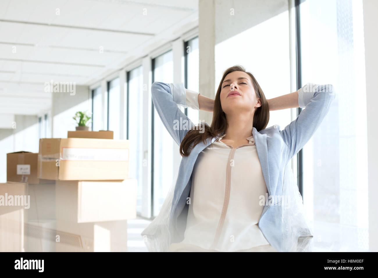 Young businesswoman détendue avec les mains derrière la tête à nouveau bureau Banque D'Images