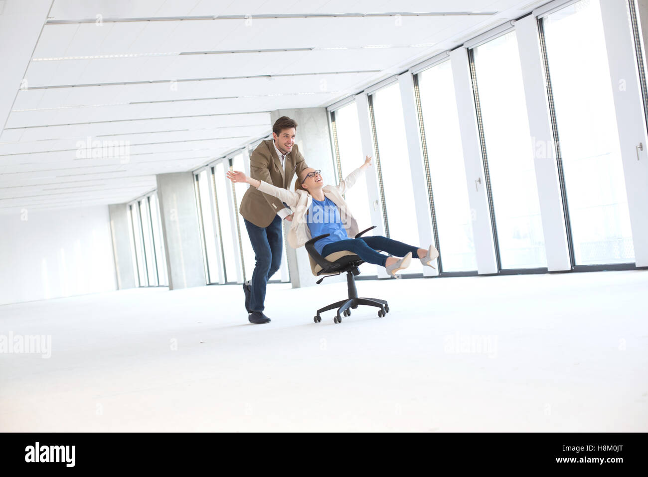 Young businessman pushing female colleague in chair at bureau vide Banque D'Images