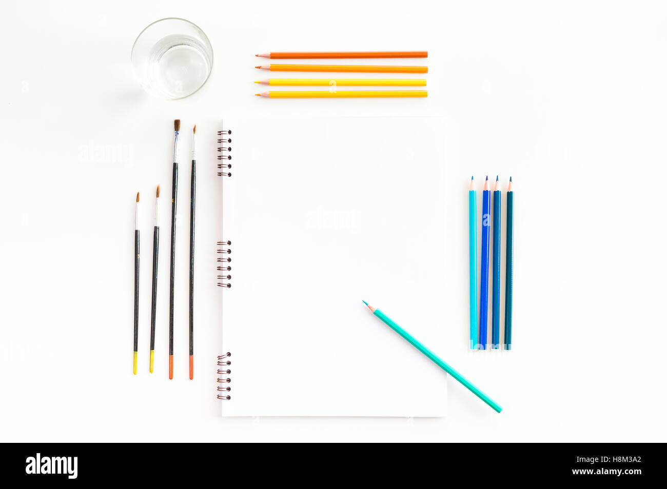 La maquette de l'art de croquis à l'aquarelle peintures, pastels, verre d'eau et un pinceaux. Vue d'en haut. Outils de travail artistique Banque D'Images