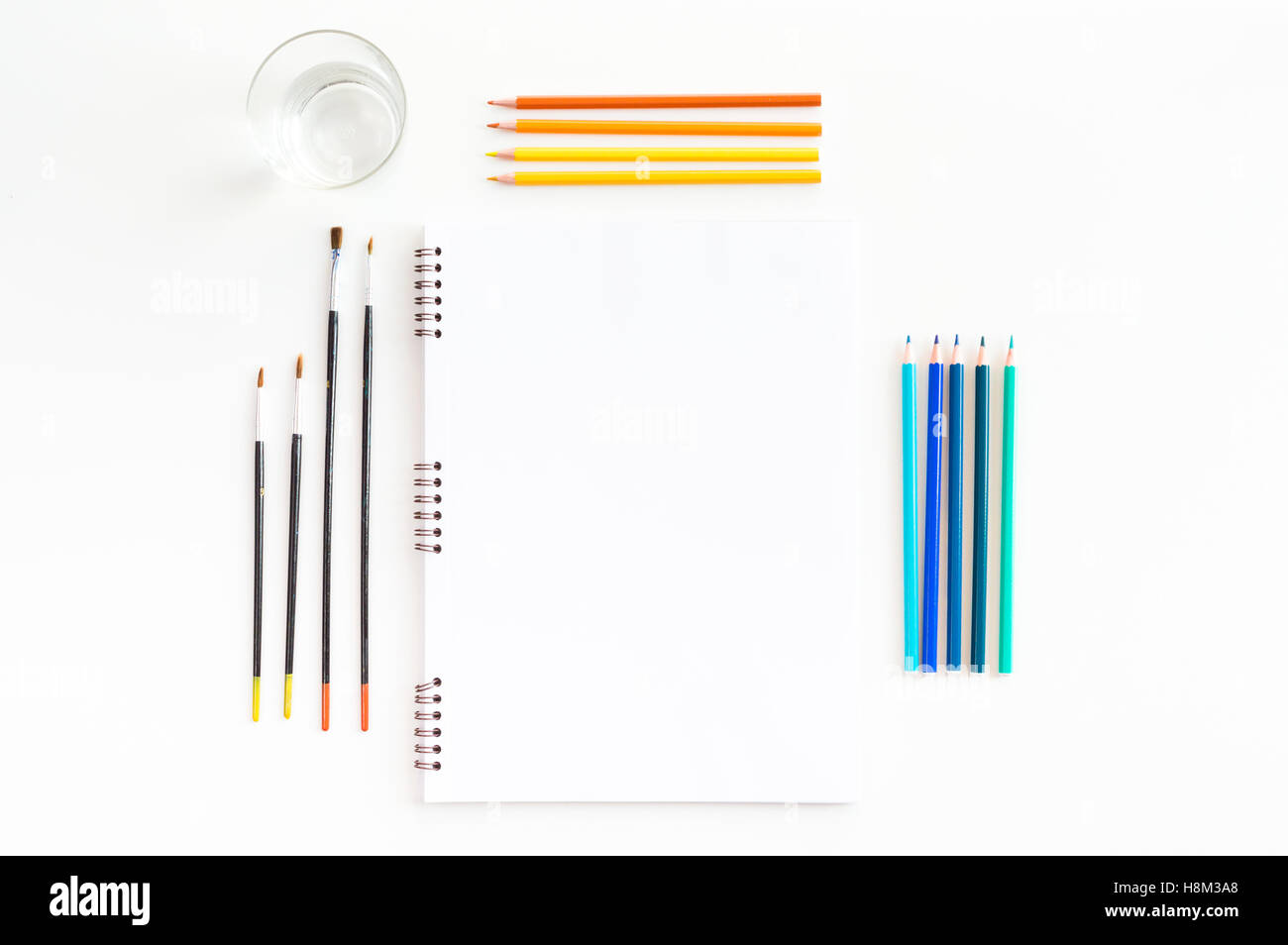 La maquette de l'art de croquis à l'aquarelle peintures, pastels, verre d'eau et un pinceaux. Vue d'en haut. Outils de travail artistique Banque D'Images