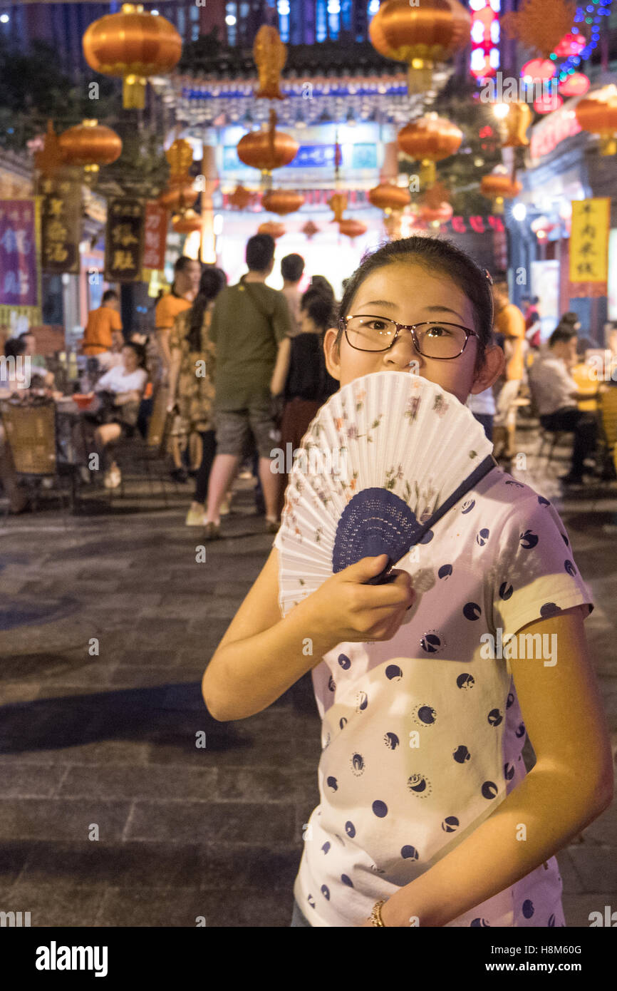 Beijing, Chine - un jeune Chinois girl holding un ventilateur en face de son visage dans le snack de Donghuamen Marché de nuit, une grande piscine m Banque D'Images