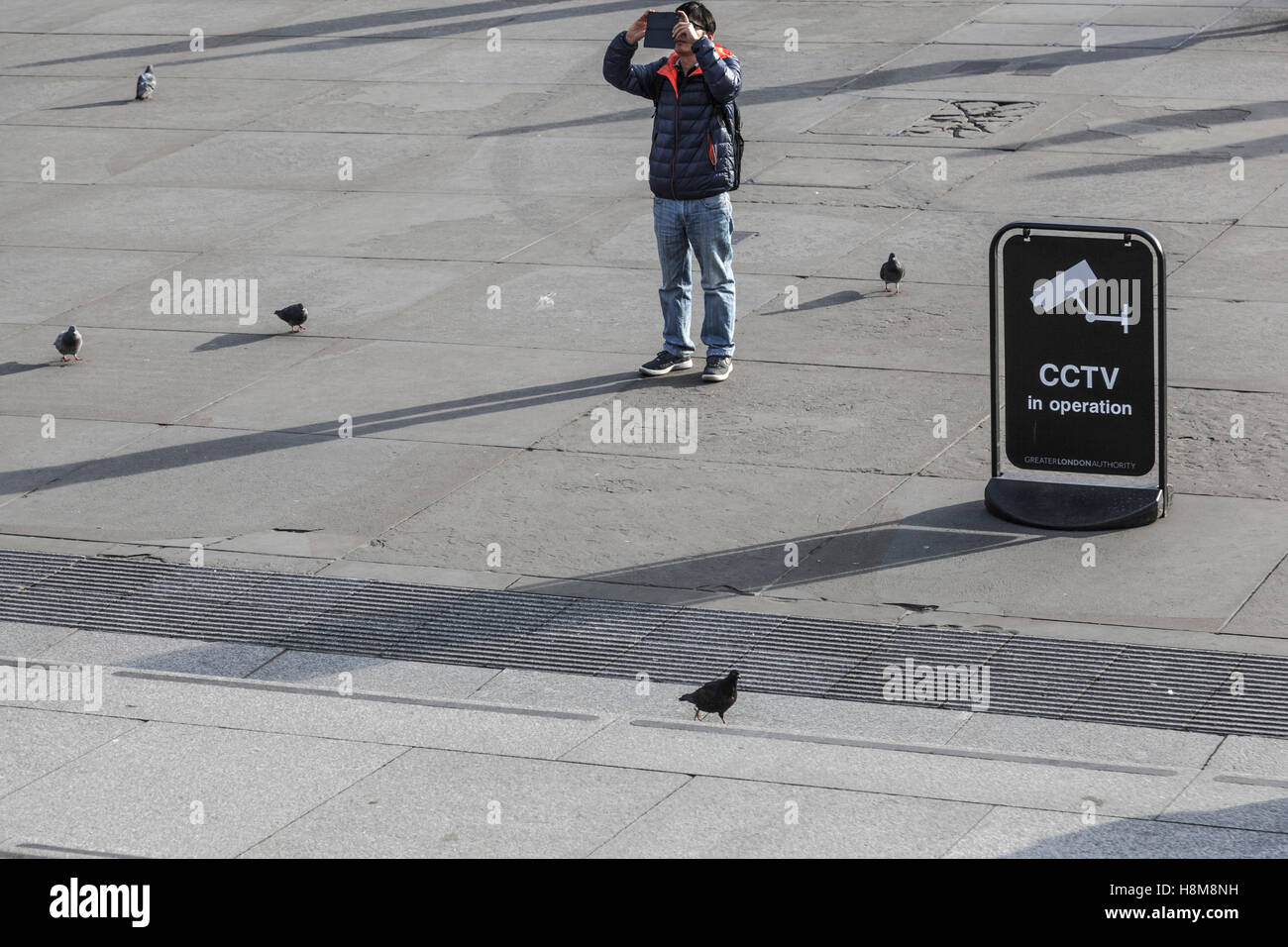 Un touriste photographie la National Gallery, Trafalgar Square en utilisant son téléphone intelligent, aux côtés d'un signe indiquant la vidéosurveillance est opérant Banque D'Images
