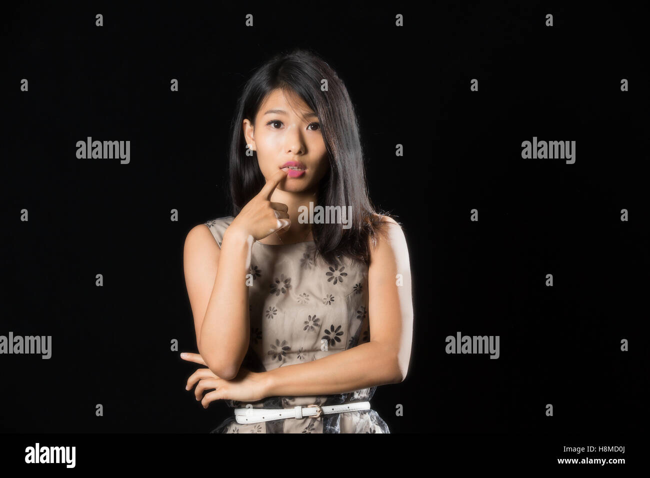 Jolie fille chinoise avec le doigt sur sa lèvre debout sur fond noir Banque D'Images