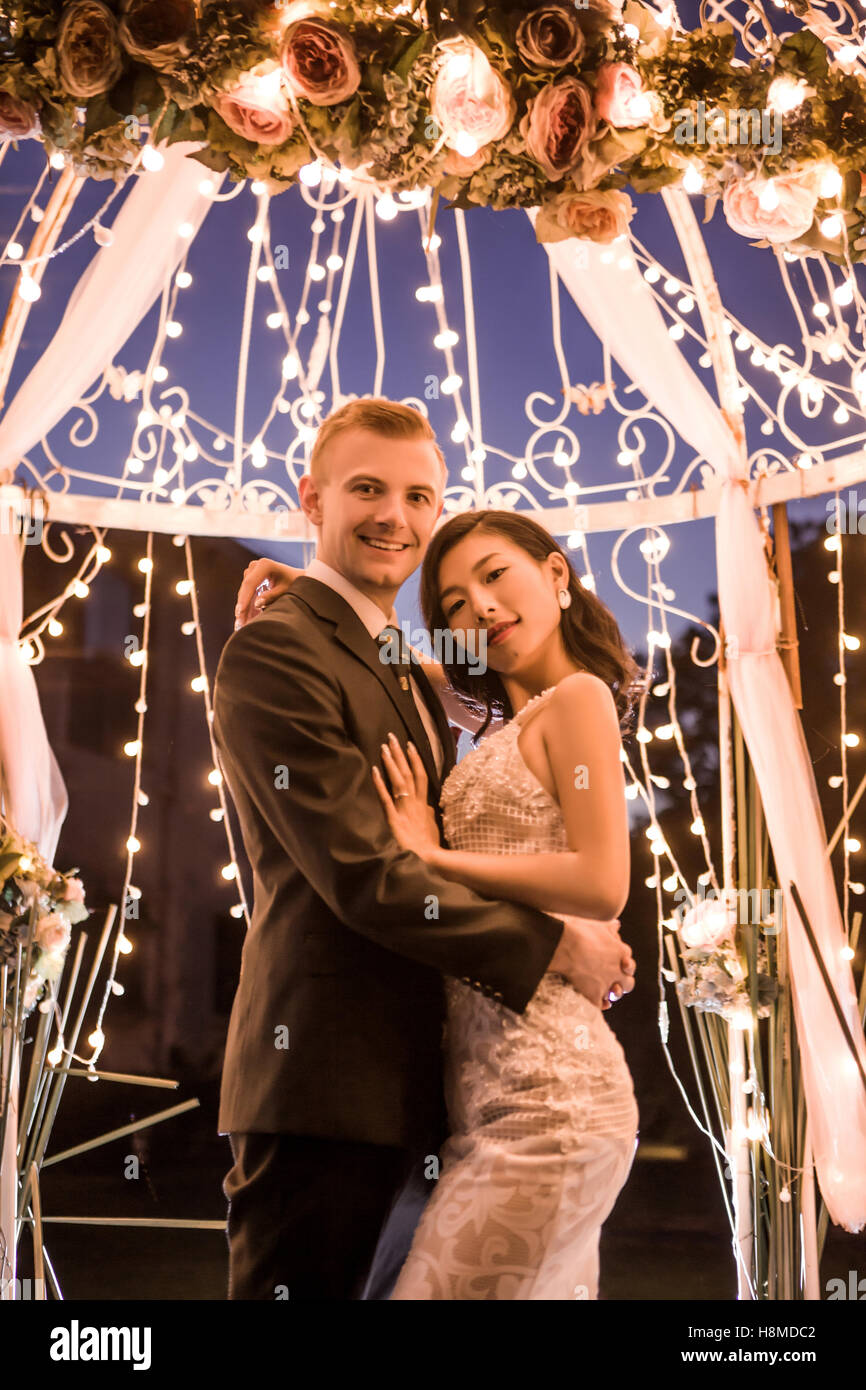 Vue de côté portrait of happy couple standing in gazebo illuminé la nuit Banque D'Images