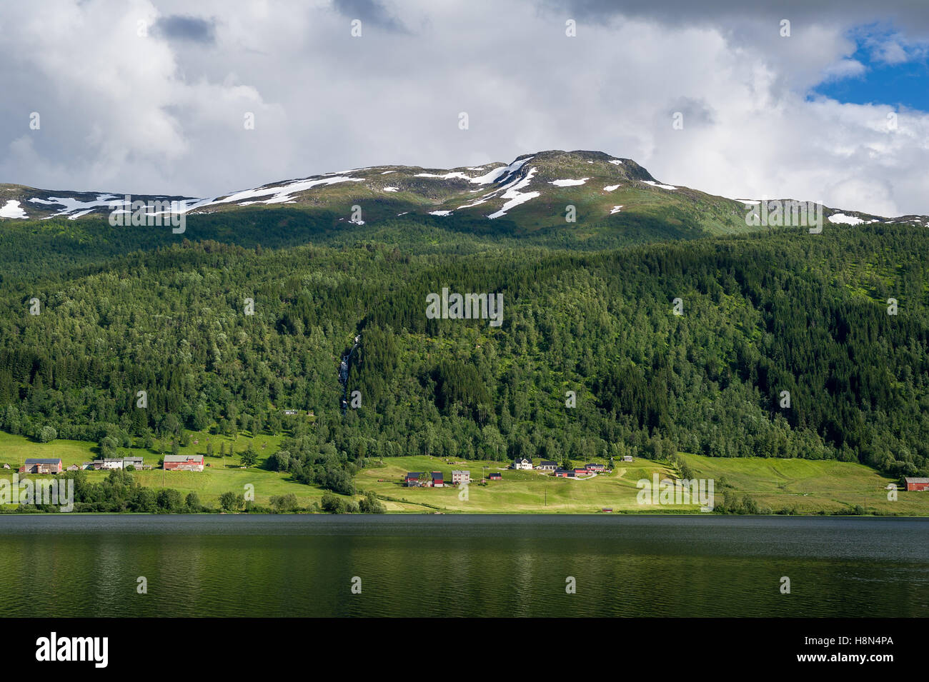 Village au bord du fjord norvégien et des sommets enneigés au-dessus. Banque D'Images