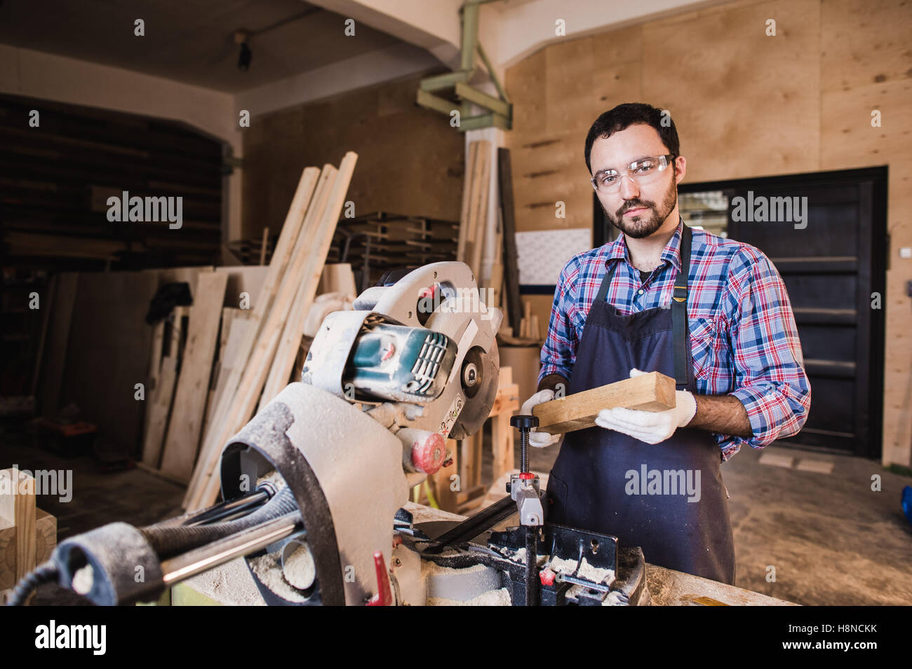Jeune artisan en uniforme travaillant à la menuiserie et à la recherche à l'appareil photo Banque D'Images