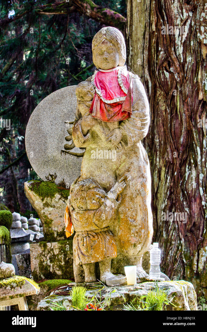 Le Japon, l'ancien cimetière Okunoin, Koyasan. Statue commémorative de graves, rouge-bibbed statue Jizo de Mère avec enfant à ses pieds accrochés à sa jupe. Banque D'Images