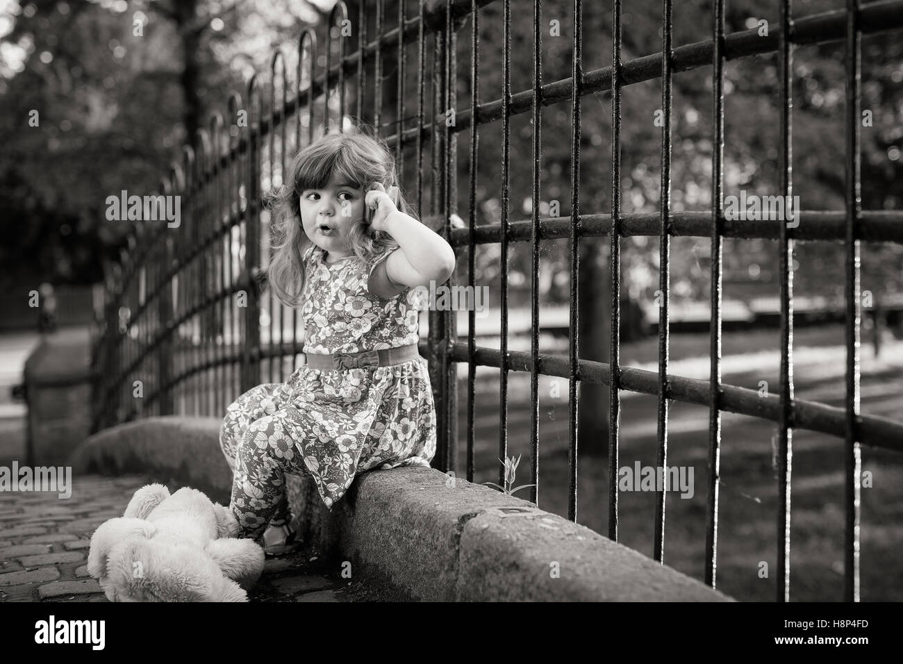 Cute little girl assis sur un pont faisant semblant de parler sur un téléphone mobile Banque D'Images