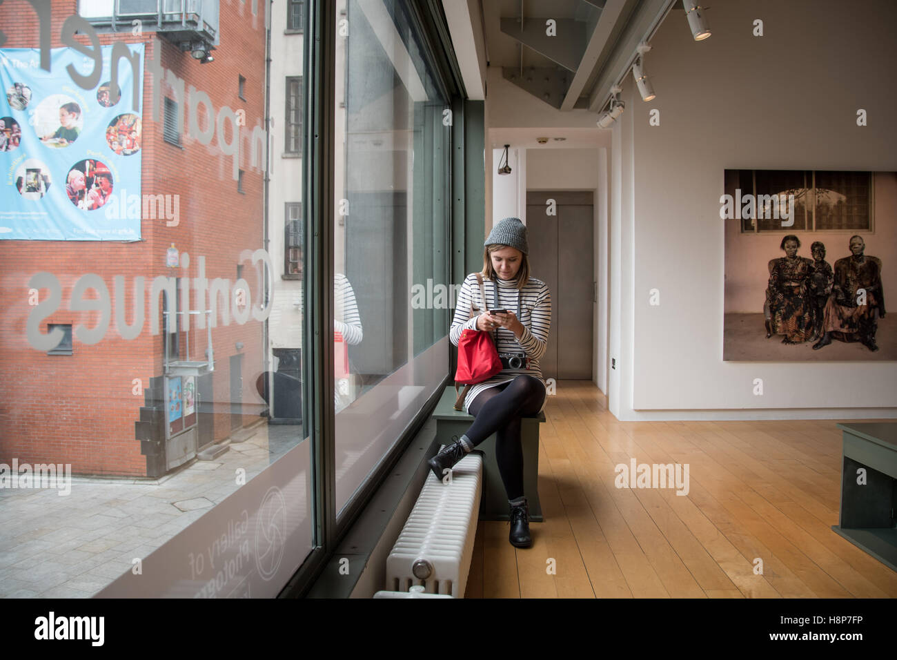 Dublin, Irlande- une jeune femme assise à l'intérieur d'une galerie d'art sur son téléphone dans la ville de Dublin. Banque D'Images