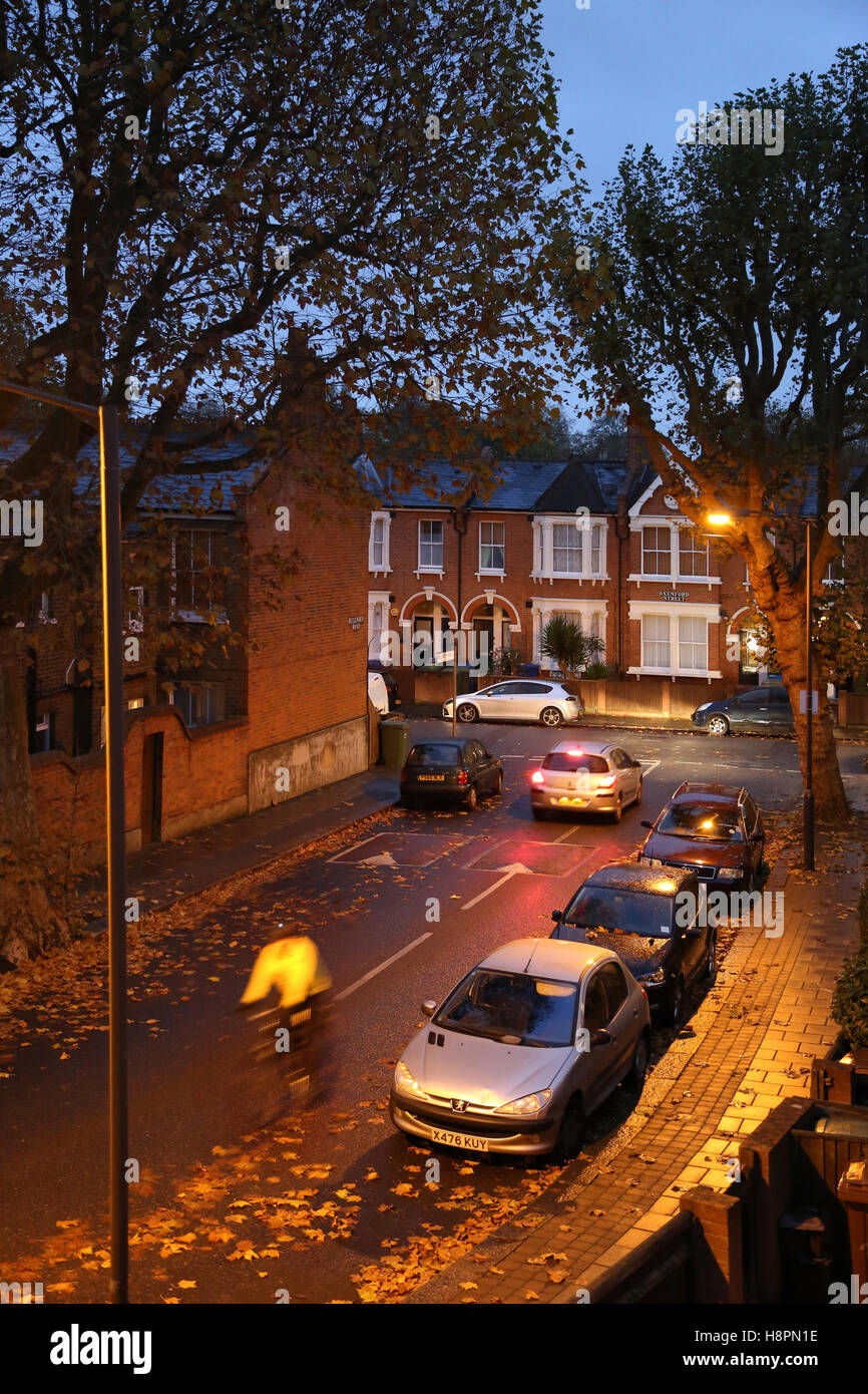 Les feuilles d'automne sur les trottoirs et les rues dans une rue typique du sud, après la tombée de la nuit à l'état humide. Un cycliste passe. Banque D'Images