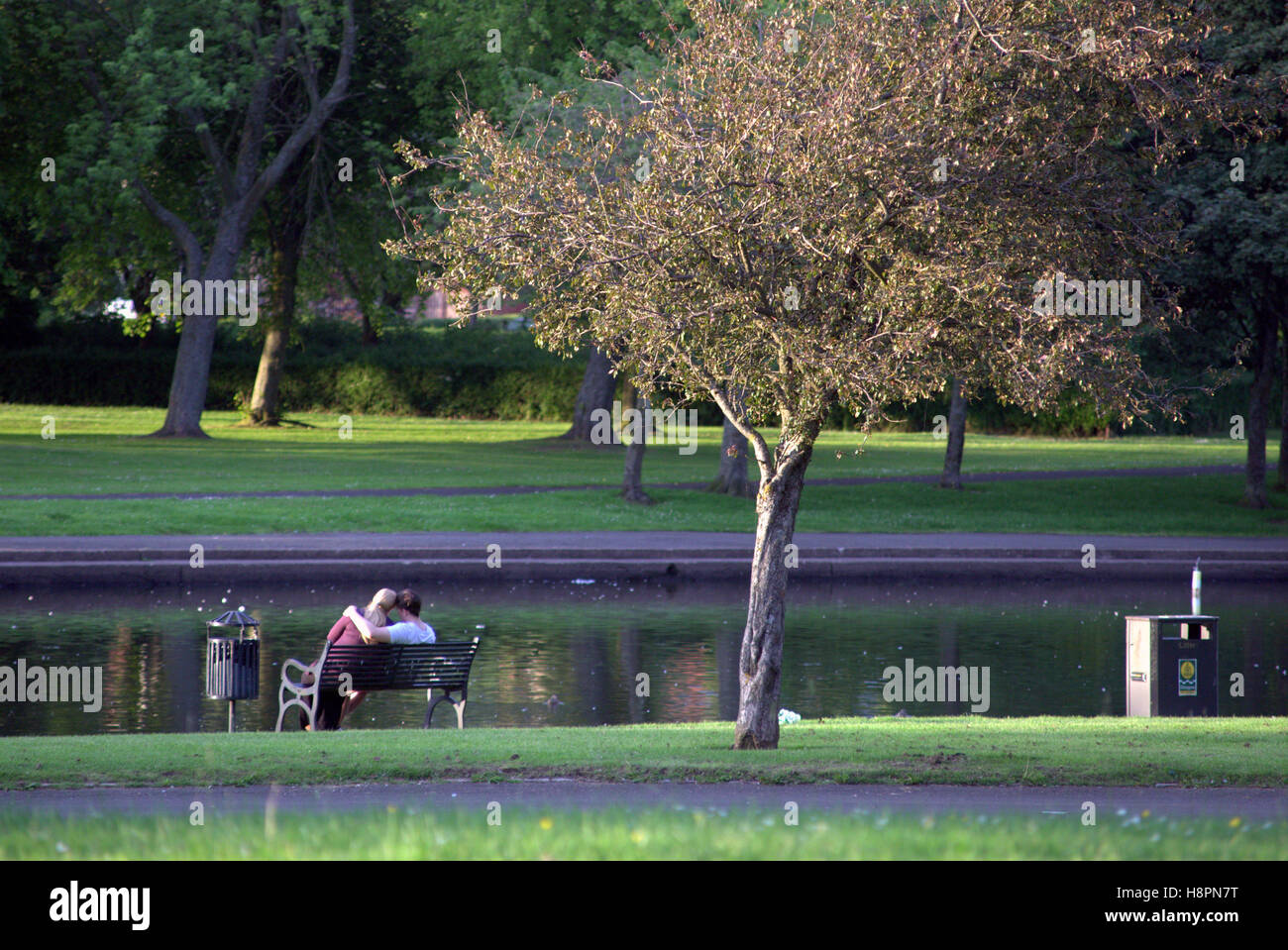 Jeune couple sur un banc de parc Knightswood étang ou lac du parc Banque D'Images