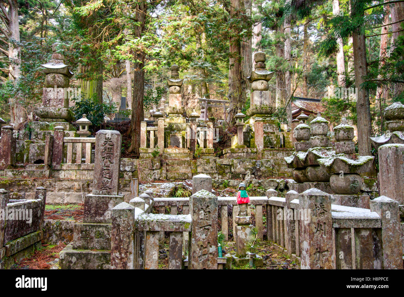 Le Japon, Koyasan, Okunoin cemetery. De nombreuses pierres memorial et cinq pagodes en pierre avec un rouge solitaire-bibbed-statue jizo. Forêt de Cèdres, arrière-plan. HDR Banque D'Images