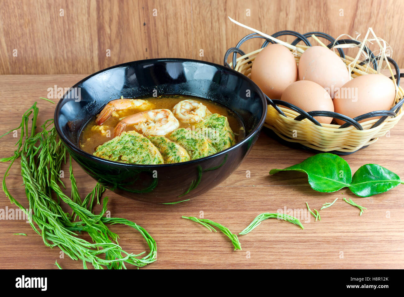 Soupe aigre et piquante curry aux crevettes et acacia pennata omelette. En noir plat sur table en bois. Banque D'Images