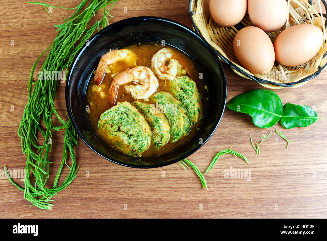 Soupe aigre et piquante curry aux crevettes et acacia pennata omelette. En noir plat sur table en bois. Banque D'Images