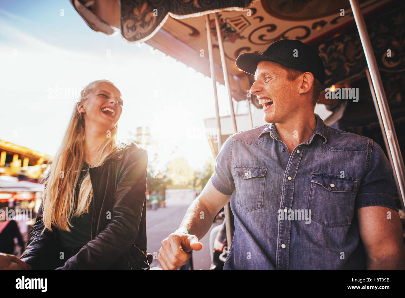 Laughing young friends riding sur carrousel dans le parc d'attractions. Smiling couple sur carousel ride. Banque D'Images