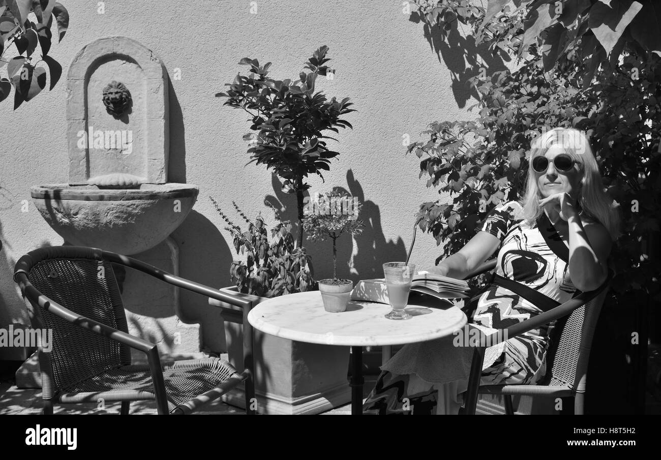 Image en niveaux de gris d'une femme, qui est assis à l'ombre avec un verre de café et lire un livre Banque D'Images