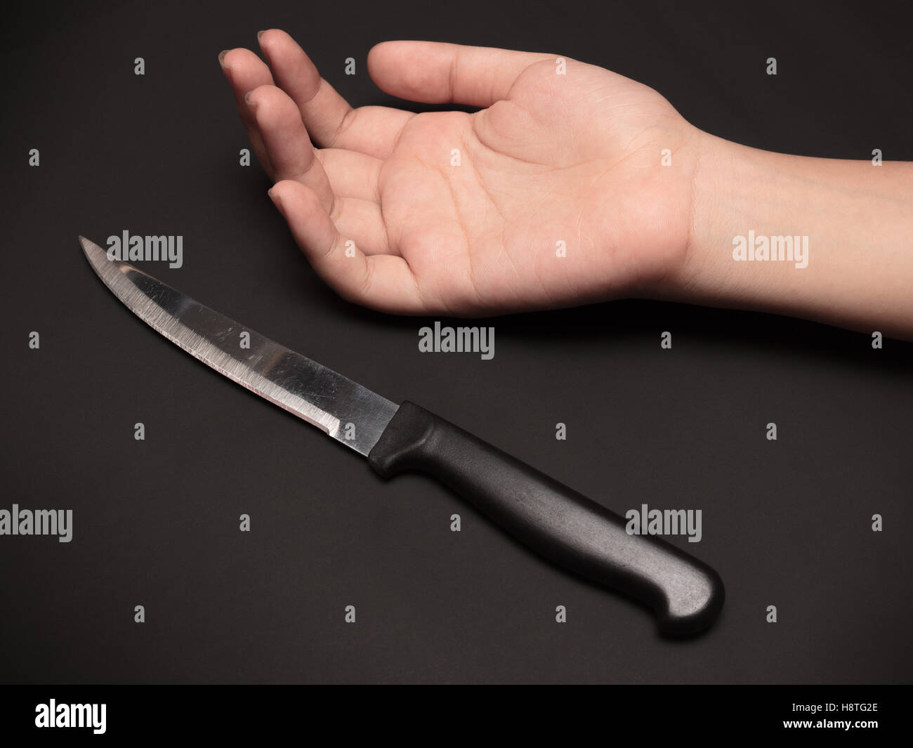 Un couteau de cuisine à côté de la main de quelqu'un sur fond sombre. Cette image a été tourné avec un seul flash bouncing technique. Banque D'Images